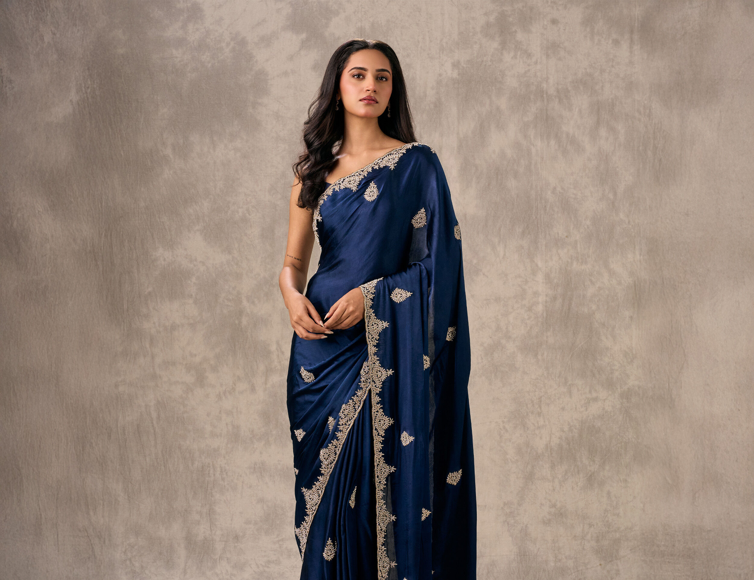 Woman in a navy blue silk saree with gold embroidery and a fitted, one-shoulder style blouse.